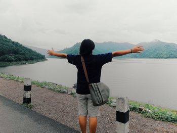 Woman with arms outstretched standing at lakeshore