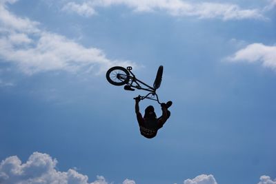 Low angle view of man with bicycle performing stunt against sky during sunny day