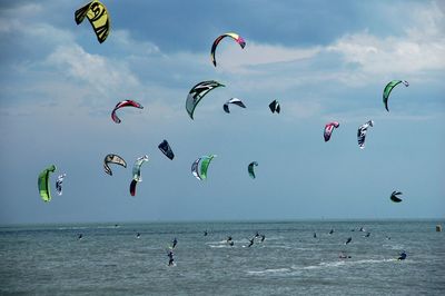 Kite surfers at beach against cloudy sky