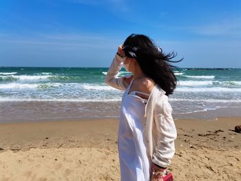 Young woman standing at beach against sky
