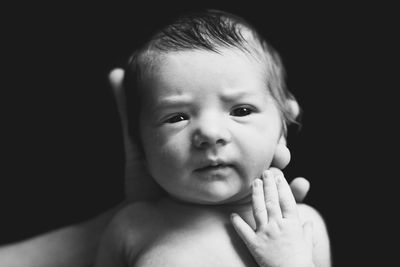 Cropped hand of parent holding baby against black background