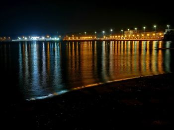 Illuminated city by river against sky at night