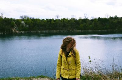 Woman shaking head while standing against lake