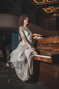 Young woman in dress sitting on piano