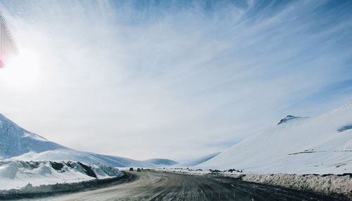 Road by mountains against sky during winter