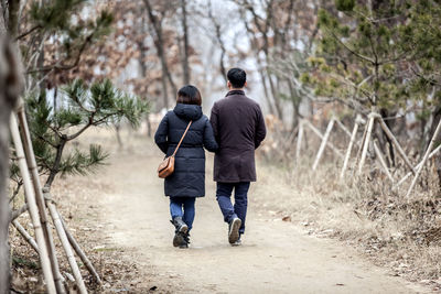 Rear view of man and woman walking on road at forest