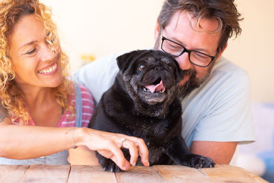 Smiling mature couple embracing pug at table