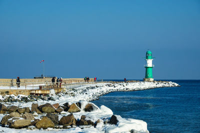 Lighthouse by sea against clear blue sky