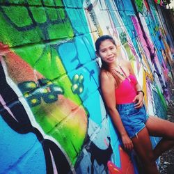 Portrait of smiling young woman standing against graffiti wall