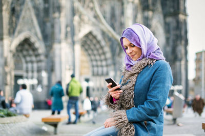 Woman holding mobile phone while standing in city