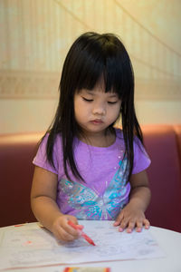 Close-up of cute girl coloring in book on table