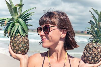 Smiling young woman holding pineapples at beach