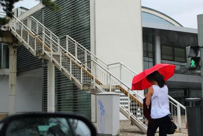 Rear view of woman with red umbrella walking in city