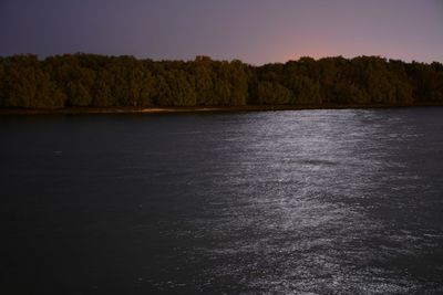 Calm lake in front of trees against clear sky