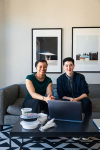 Portrait of confident smiling business coworkers with laptop at table sitting in office