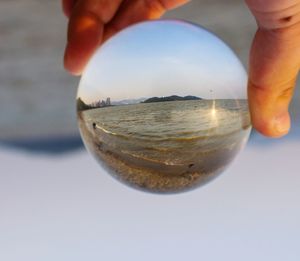 Close-up of hand holding crystal ball against sea