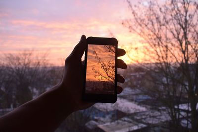 Close-up of hand holding smart phone against sunset sky