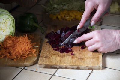 A woman cuts beets in the kitchen against the background of fresh vegetables