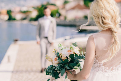 Rear view of bride holding bouquet while groom standing in background