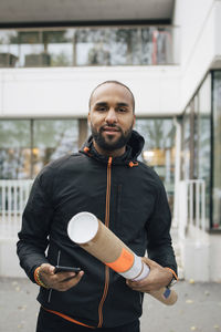 Portrait of male messenger holding package and smart phone in city