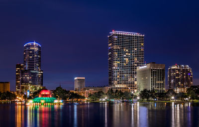 Illuminated city by river against sky at night