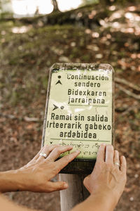 From above cropped anonymous blind elderly traveler touching and reading braille on signboard while visiting park on summer weekend day