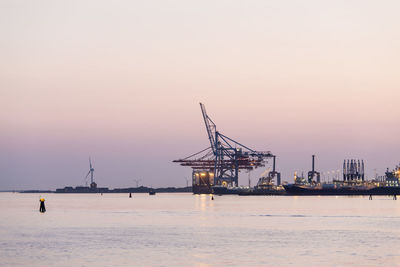 Cranes by river against sky during sunset