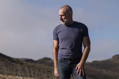 Adult man in jeans against sky and mountain on a sunny day