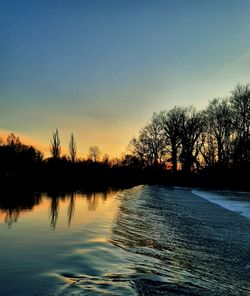 Silhouette trees by lake against sky during sunset