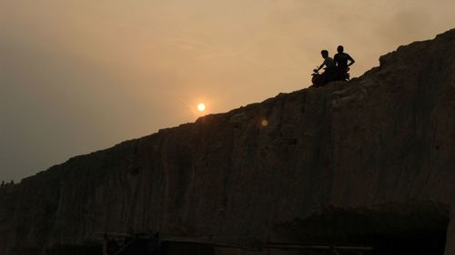 Low angle view of silhouette man on cliff against sky during sunset