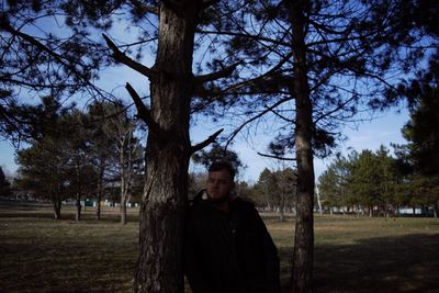 Portrait of young man standing by tree on field