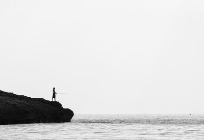 Man standing on rock by sea against clear sky