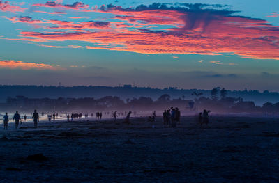 Silhouette people on landscape against sky during sunset