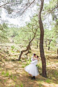 Woman standing by tree on field in forest
