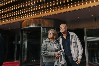 Smiling male and female senior friends standing outside movie theater