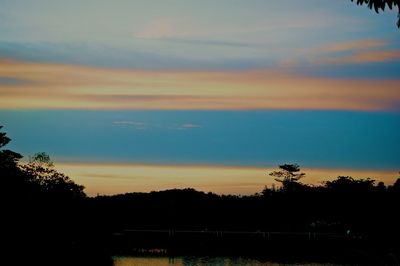 Silhouette trees on landscape against sky at sunset