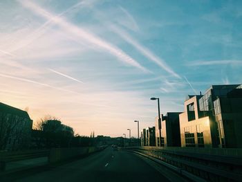 Road by buildings against sky during sunset