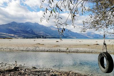 Scenic view of mountains, lake and tire swing against sky