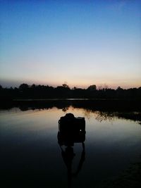 Silhouette camera on lake against clear sky during sunset