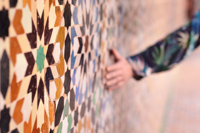 Cropped hand of person touching mosaic wall