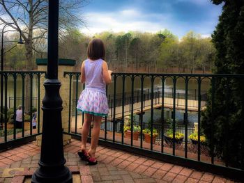 Rear view of woman standing by railing against trees