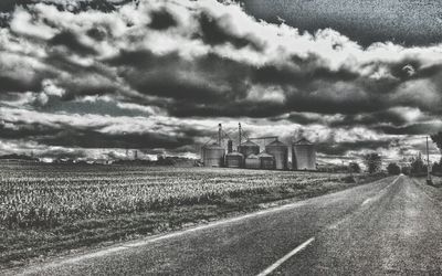 Road passing through field against cloudy sky