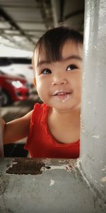 Cute baby girl looking away while standing by pillar