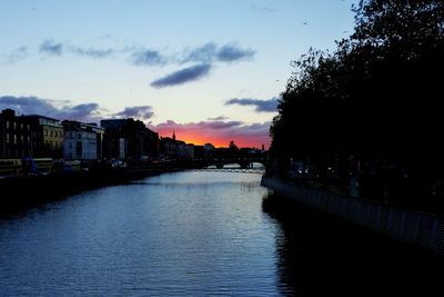 River by silhouette city against sky at sunset