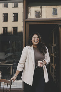 Happy businesswoman holding coffee cup standing near office doorway