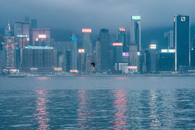 Illuminated buildings by sea against sky at night