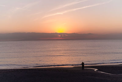 Silhouette person standing on beach against sky during sunset