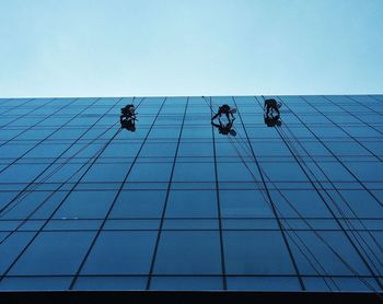 Low angle view of workers cleaning buildings against clear sky