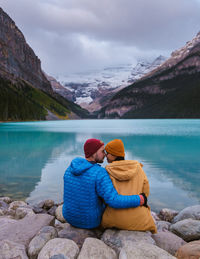 Rear view of woman sitting on rock by lake against mountain