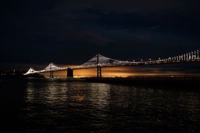 Illuminated bridge over river against sky at night